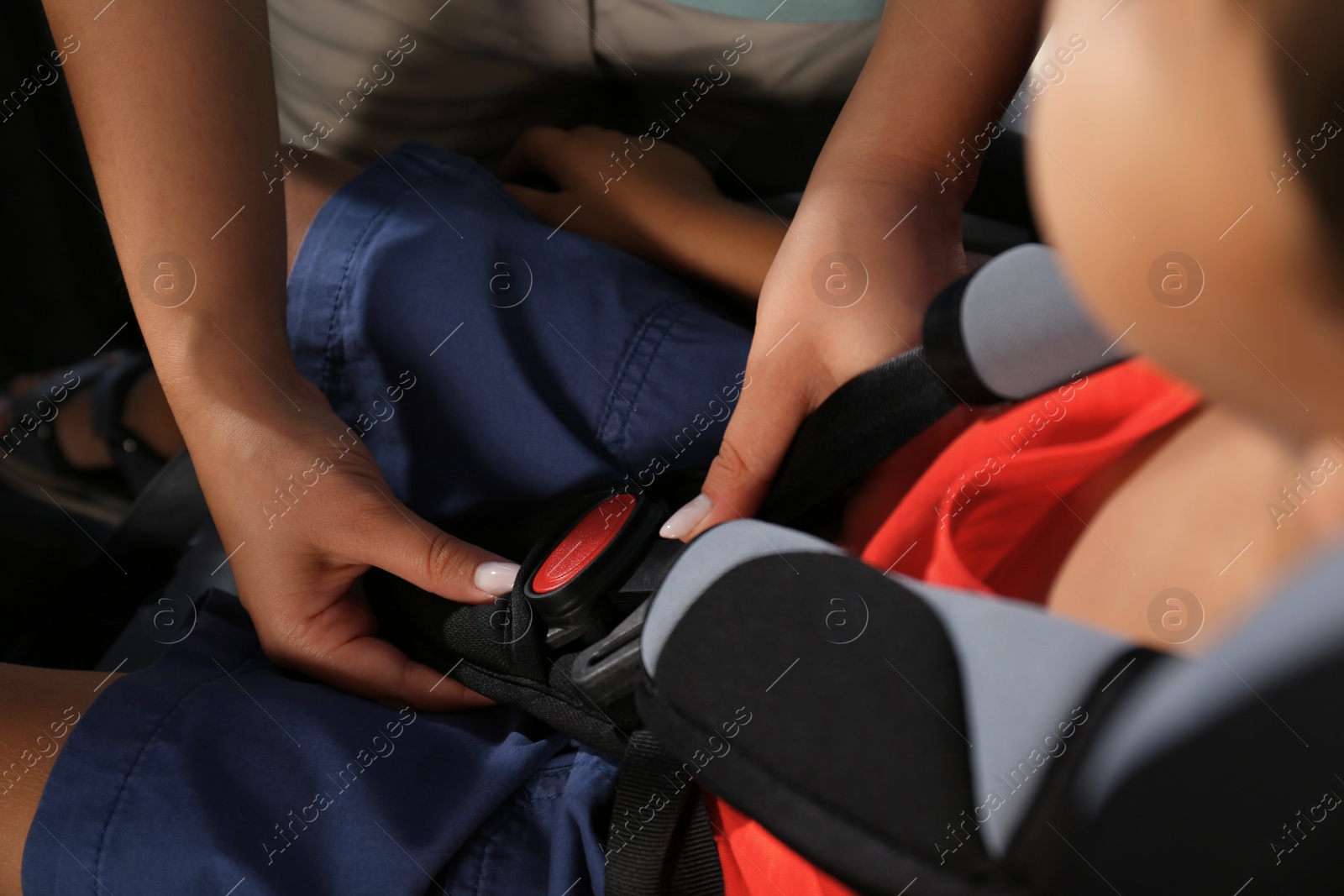 Photo of Mother fastening her son with car safety belt in child seat, closeup