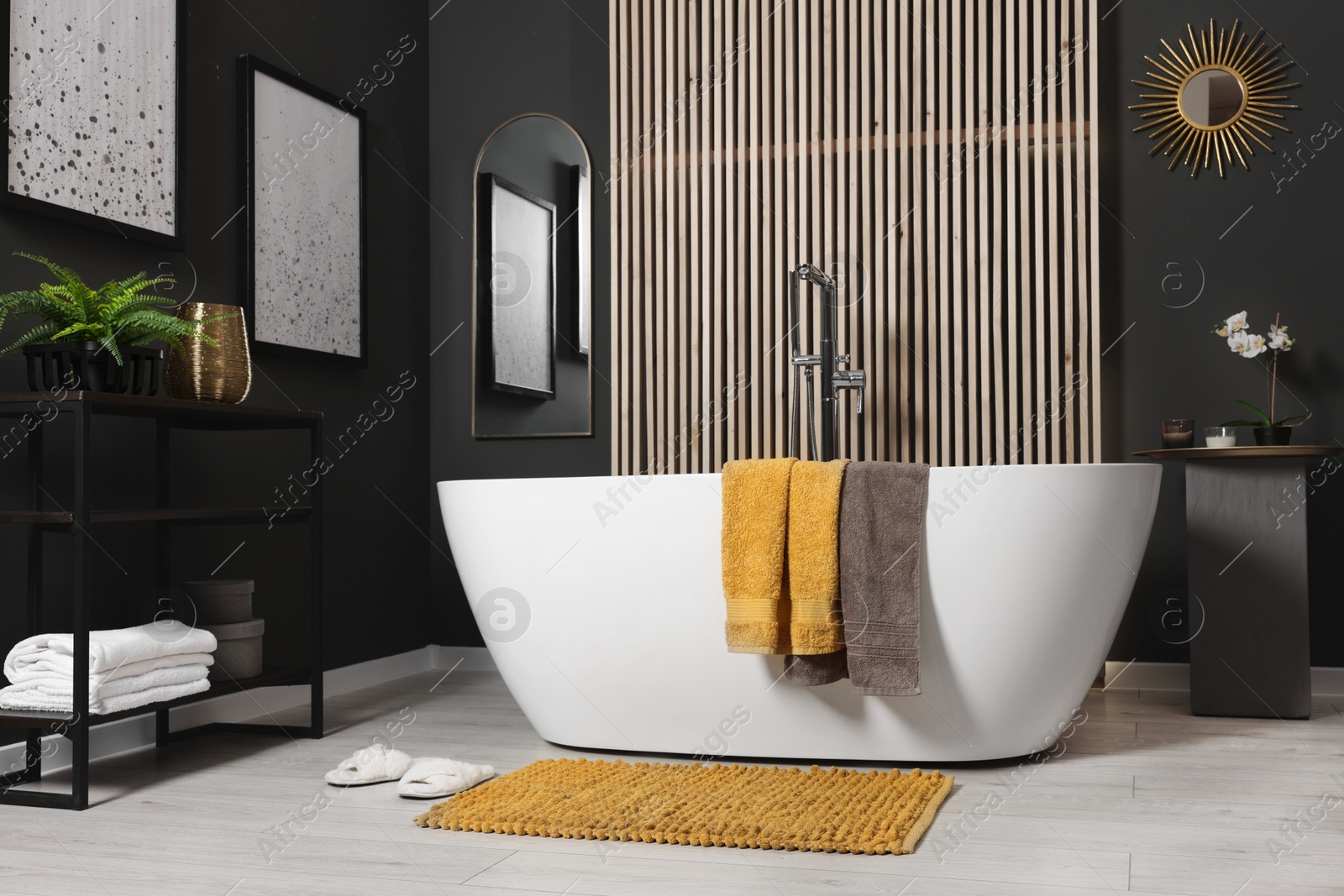 Photo of Stylish bathroom interior with bath tub, houseplants and soft yellow mat