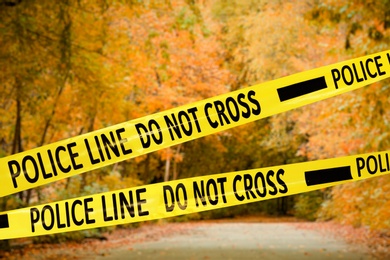 Image of Yellow police tape isolating crime scene. Blurred view of autumn park 