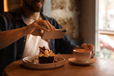 Photo of Young blogger taking picture of dessert and coffee at table in cafe, closeup