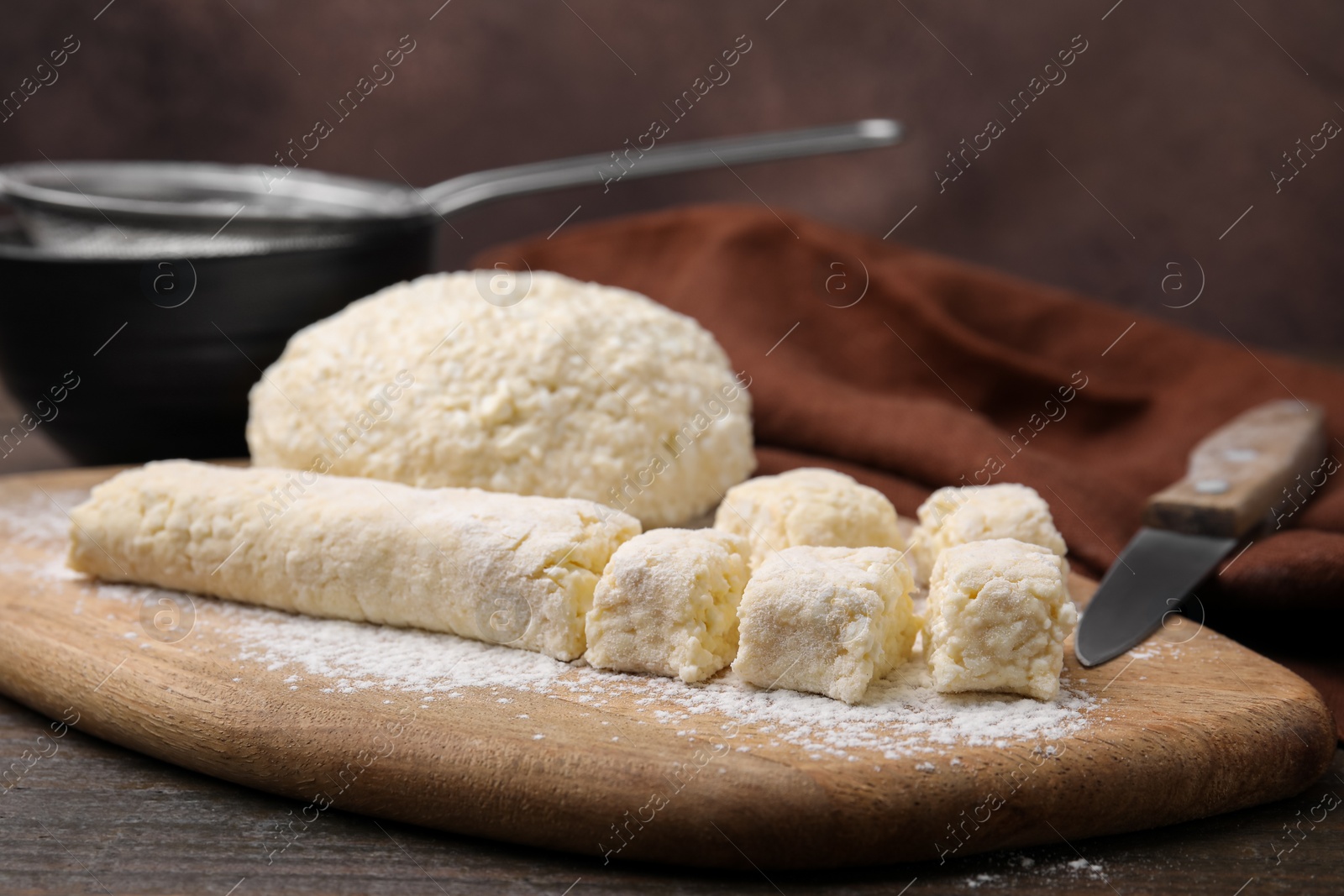 Photo of Making lazy dumplings. Board with raw dough, flour and knife on wooden table, closeup