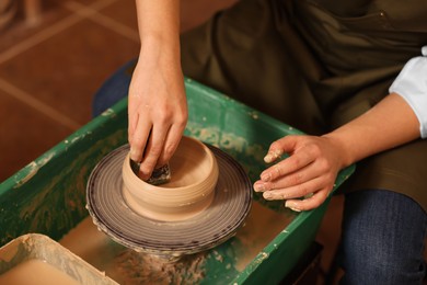 Photo of Clay crafting. Woman making bowl on potter's wheel indoors, closeup