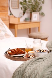 Wooden tray with delicious breakfast on bed indoors, space for text