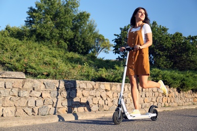 Young woman riding kick scooter along city street