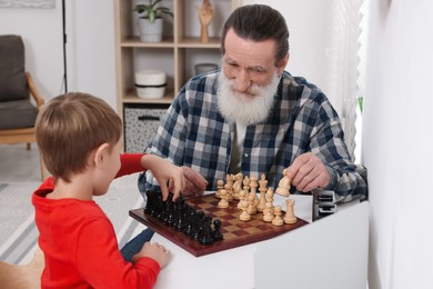 Photo of Grandfather and grandson playing chess at table in room