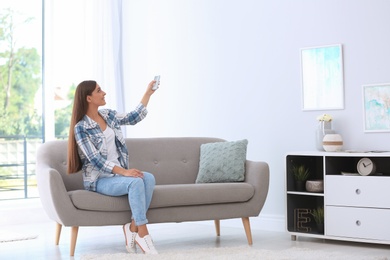 Photo of Young woman with air conditioner remote at home