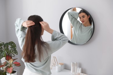 Photo of Young woman doing hair near mirror at home. Morning routine