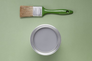 Photo of Can with gray paint and brush on light green background, flat lay