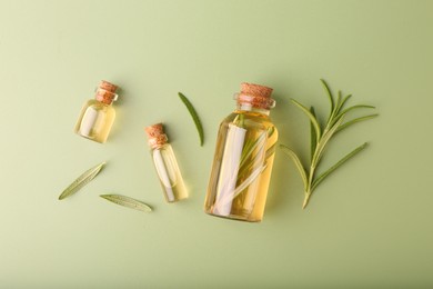 Aromatic essential oils in bottles and rosemary on green background, flat lay