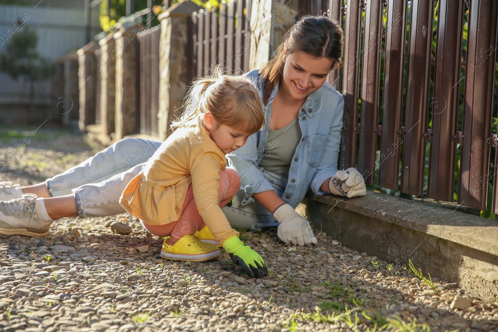 Photo of Mother and her cute daughter spending time together while pulling out grass near house on spring day