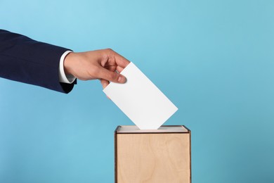 Photo of Man putting his vote into ballot box on light blue background, closeup