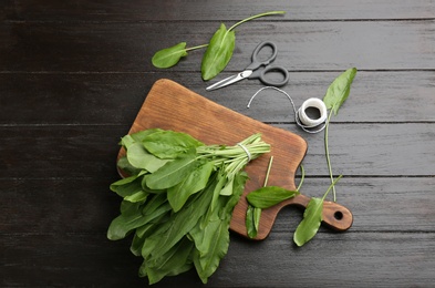 Photo of Fresh green sorrel leaves, scissors and thread on black wooden table, flat lay
