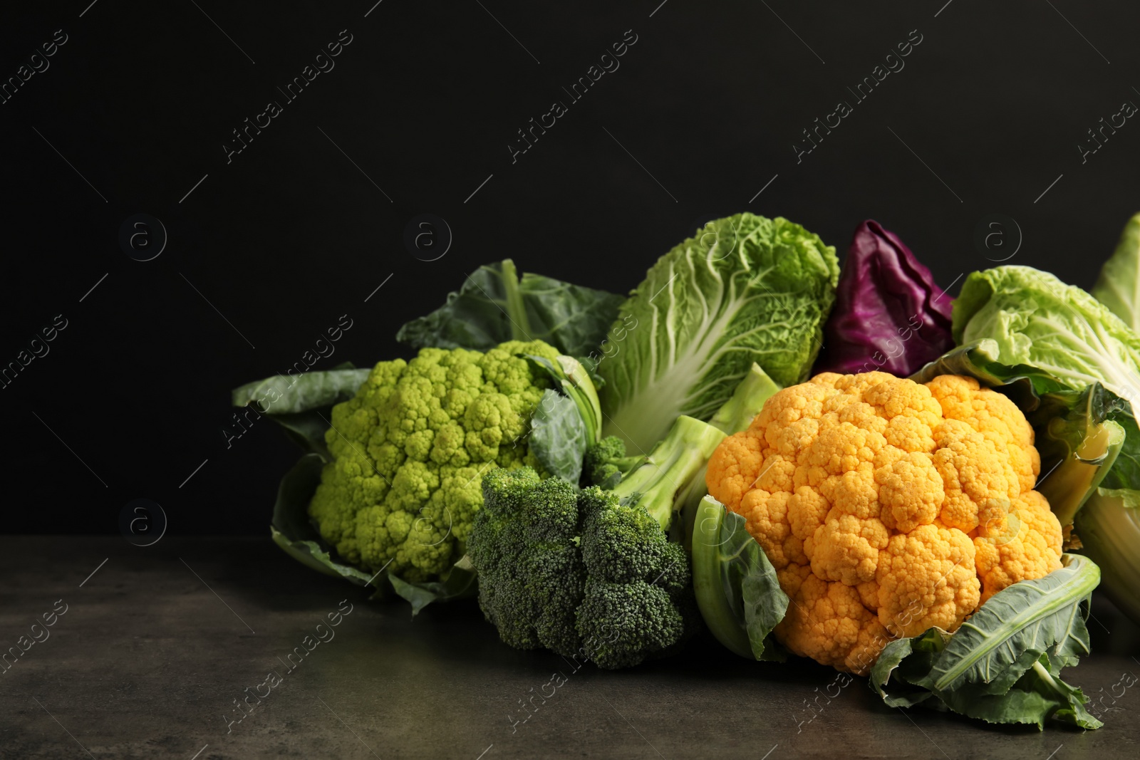 Photo of Different fresh cabbages on table against black background. Healthy food