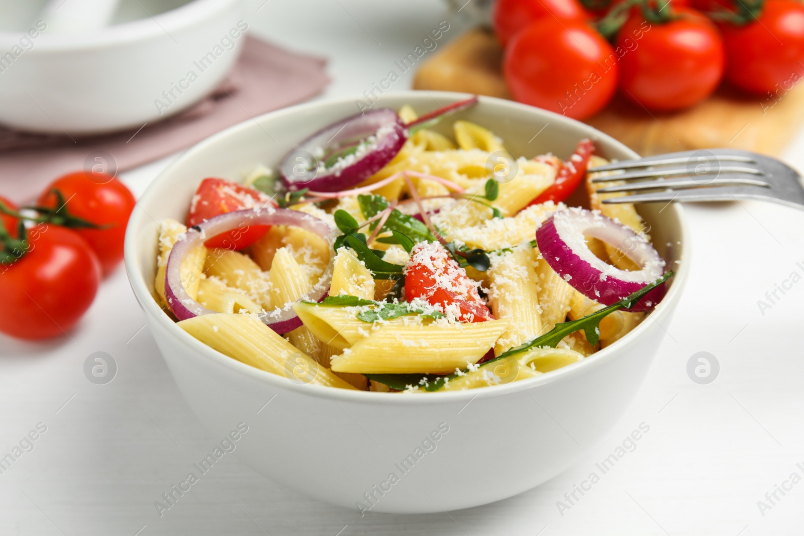 Photo of Bowl of delicious pasta with tomatoes, onion and cheese on white wooden table, closeup