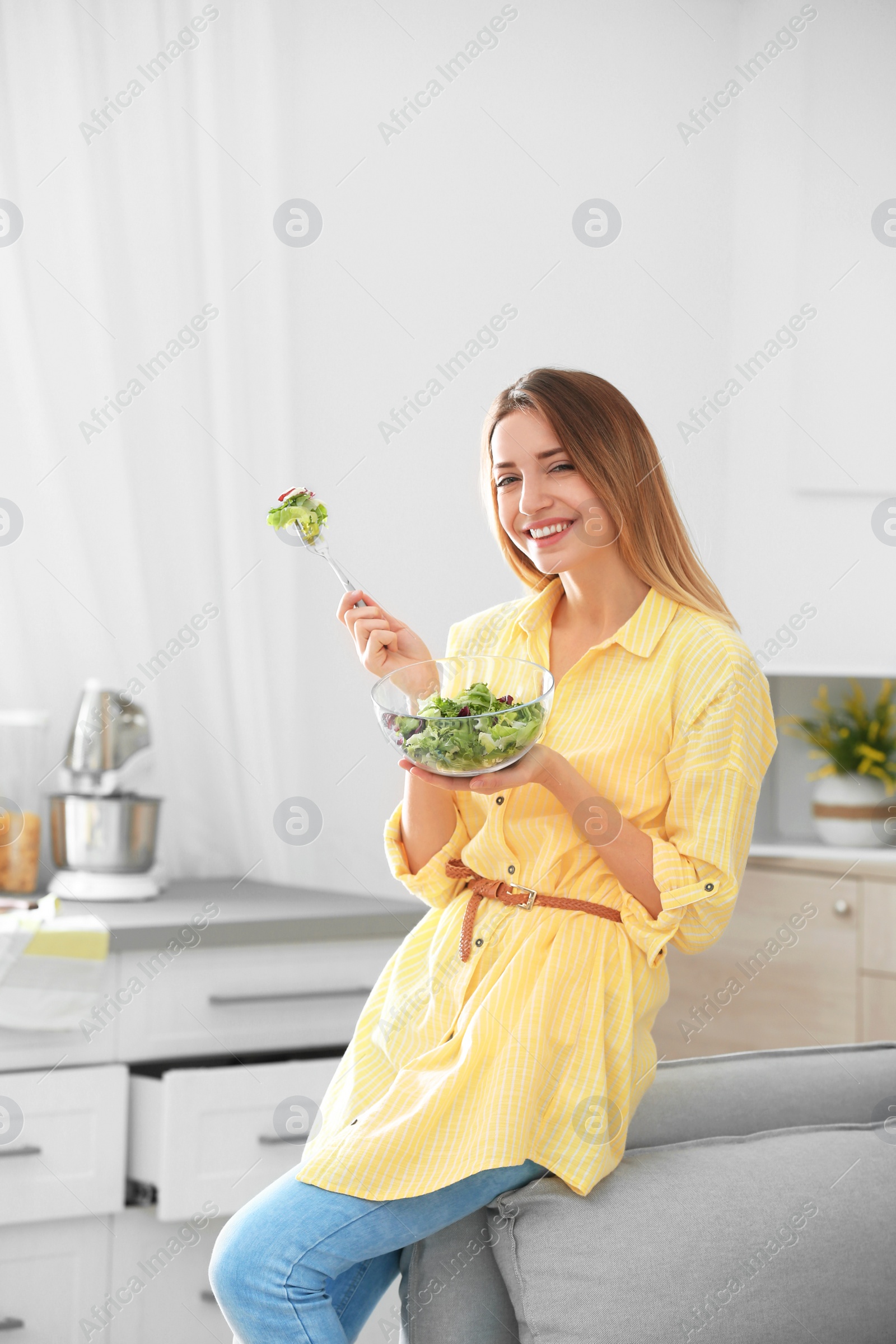 Photo of Happy young woman eating salad in kitchen. Healthy diet