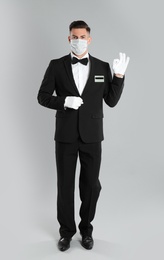 Photo of Waiter wearing medical face mask on light grey background