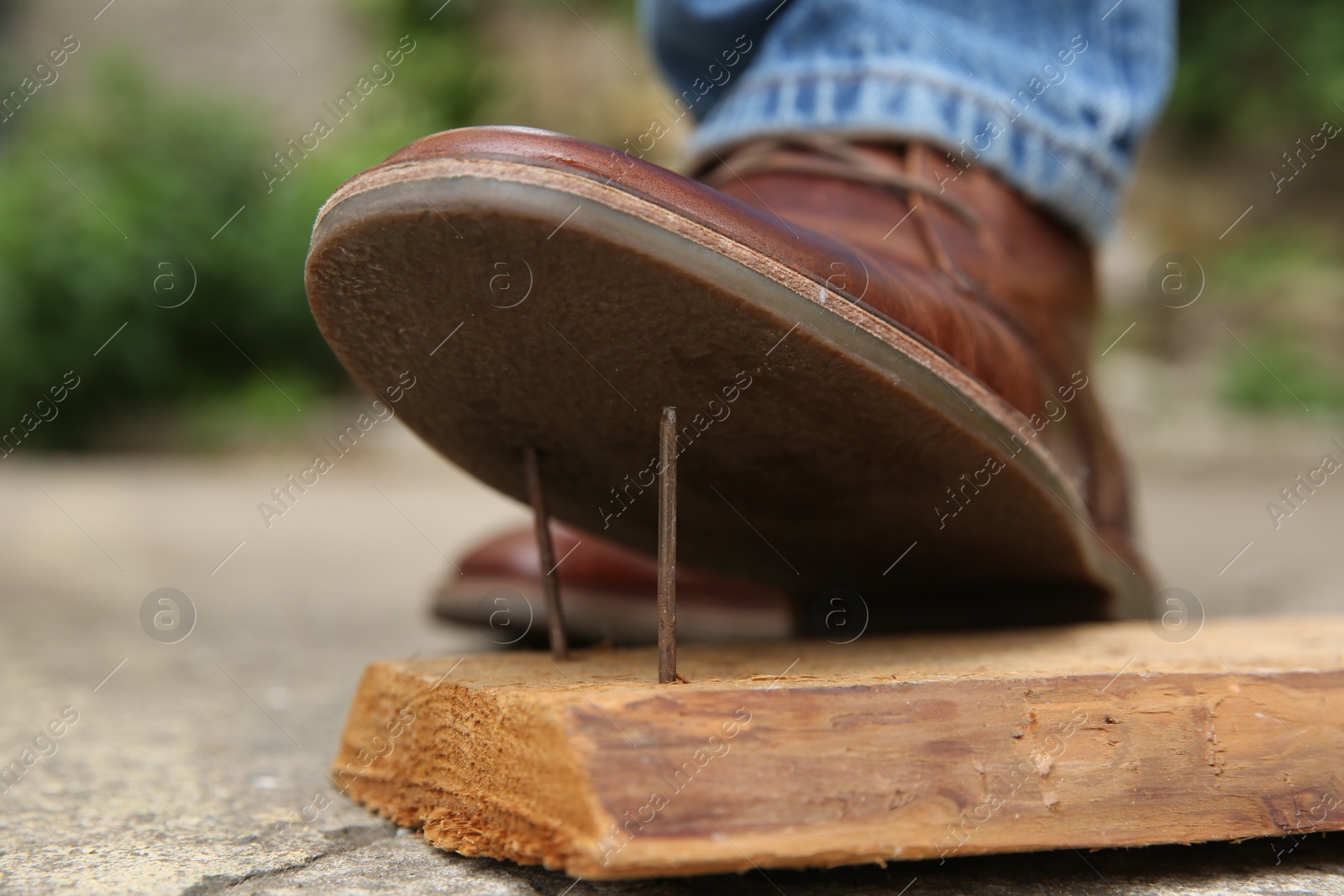 Photo of Careless man stepping on nails in wooden plank outdoors, closeup