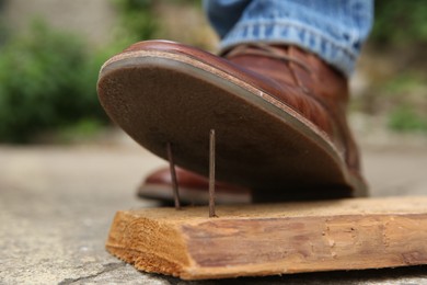 Careless man stepping on nails in wooden plank outdoors, closeup