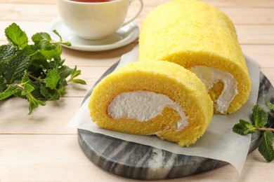 Delicious cake roll and mint on light wooden table, closeup