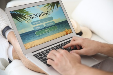 Photo of Man booking tickets online on sofa indoors, closeup. Travel agency concept