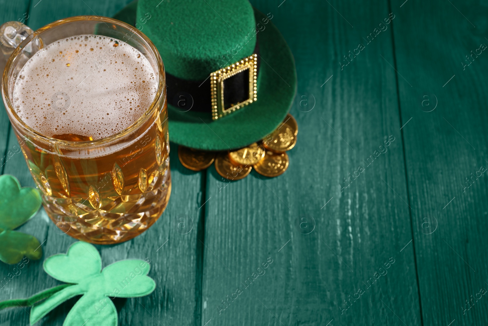 Image of St. Patrick's day. Beer, leprechaun hat, gold and decorative clover leaves on green wooden table. Space for text