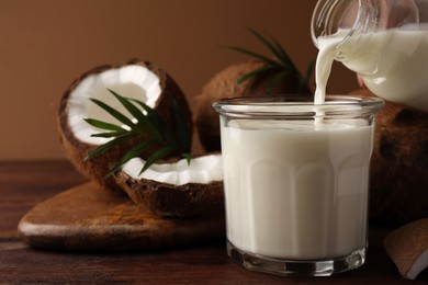 Pouring delicious coconut milk into glass on wooden table