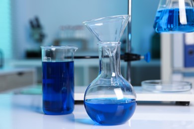 Laboratory analysis. Flasks and beaker with blue liquid on white table indoors