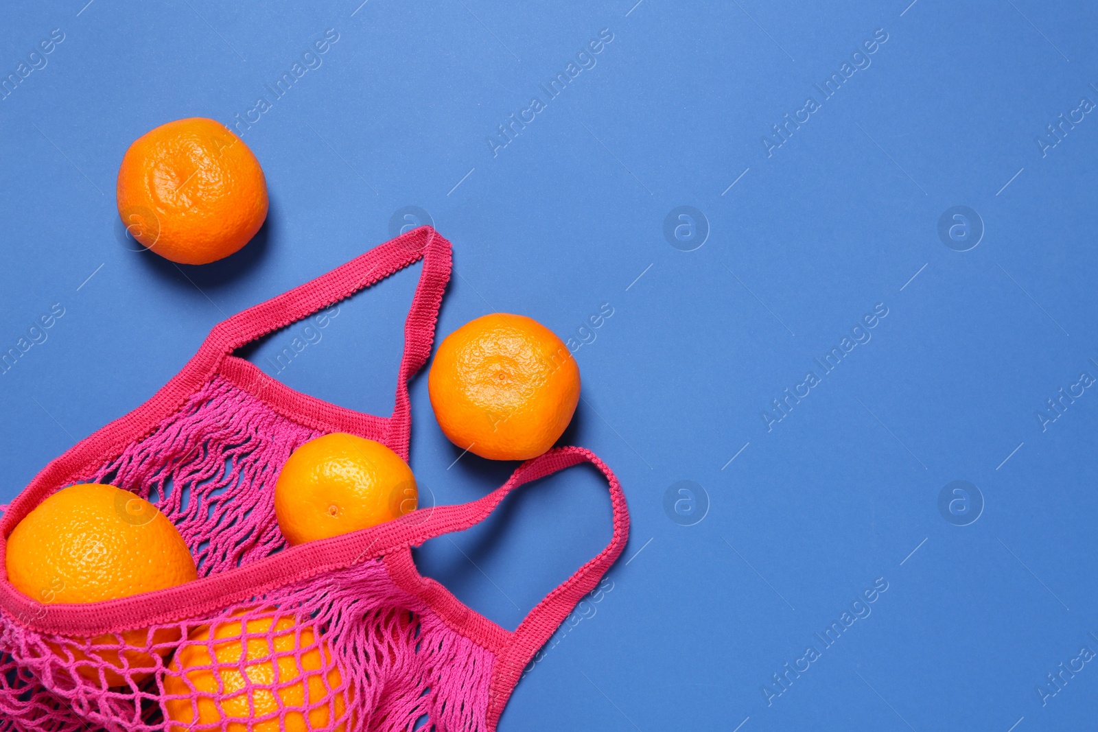 Photo of Pink net bag with citrus fruits on blue background, flat lay. Space for text