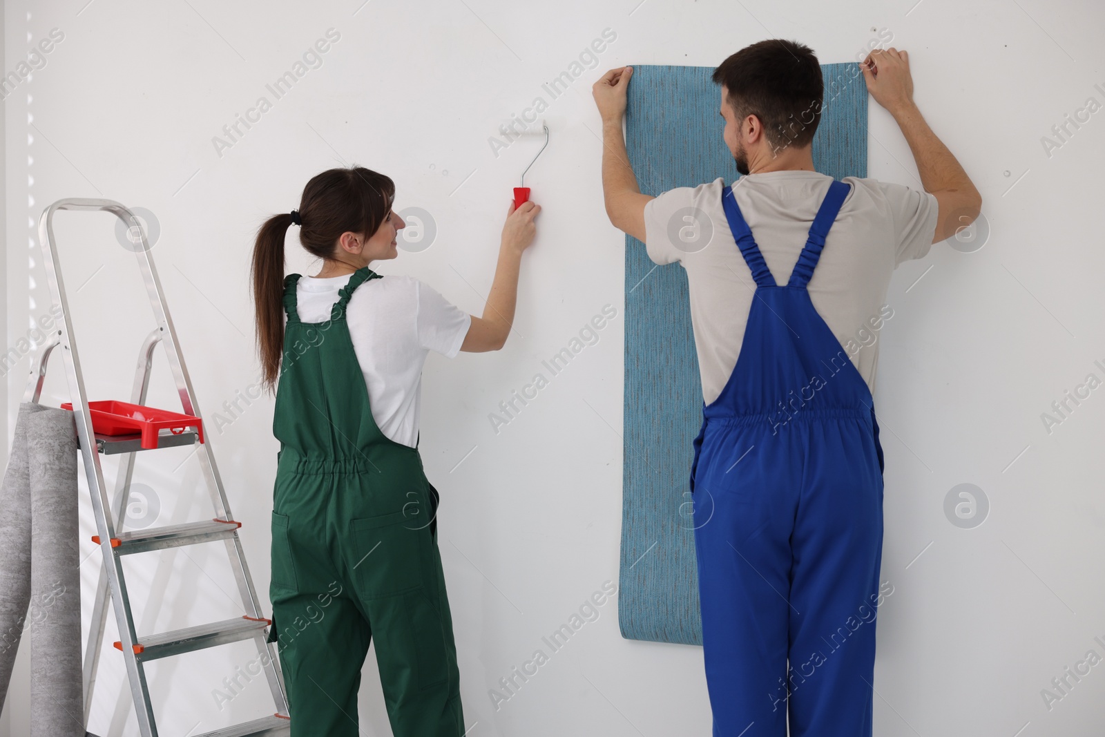 Photo of Workers hanging light blue wallpaper in room