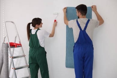 Photo of Workers hanging light blue wallpaper in room