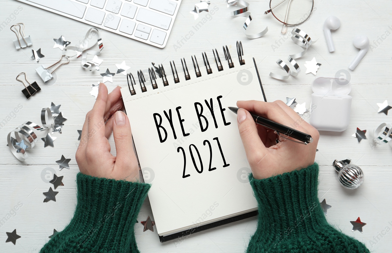 Image of Woman writing phrase Bye Bye 2021 in notebook at white wooden table, top view