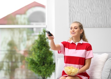 Woman watching TV with bowl of potato chips in living room. Space for text