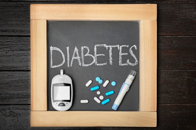 Photo of Blackboard with word "Diabetes", digital glucometer and medicine on wooden background