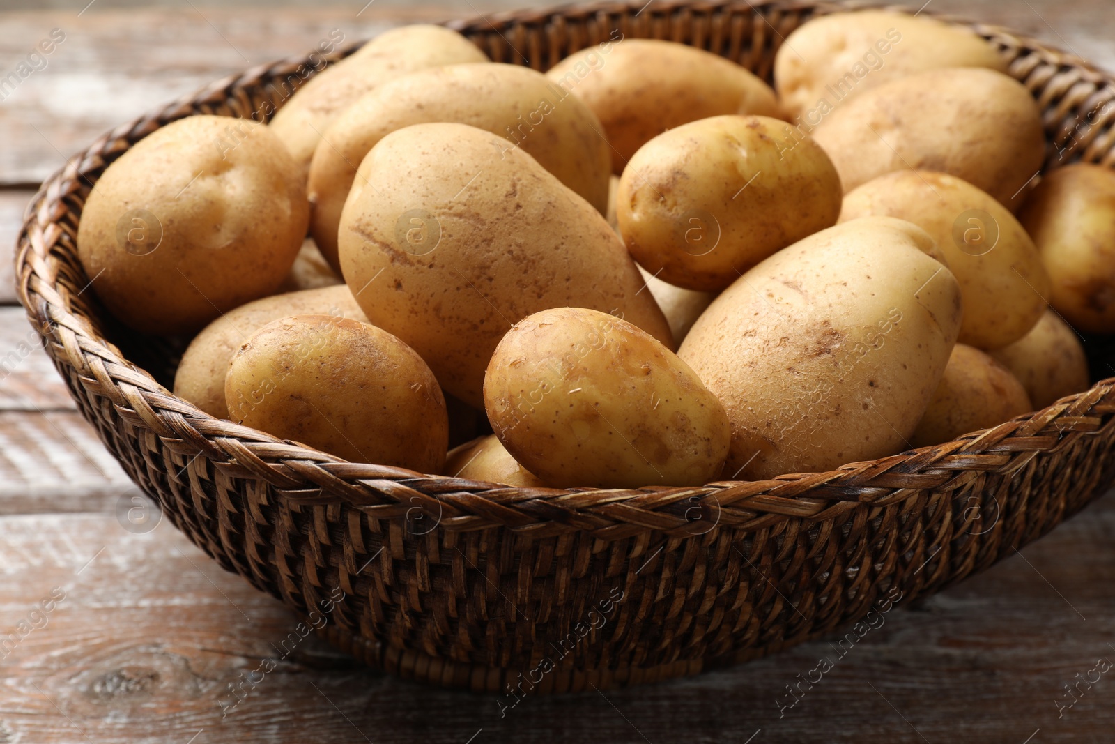 Photo of Raw fresh potatoes in wicker basket on wooden table, closeup