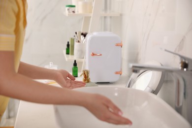 Photo of Woman washing hands near cosmetic refrigerator in bathroom