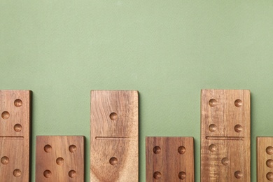Photo of Wooden domino tiles on green background, flat lay. Space for text