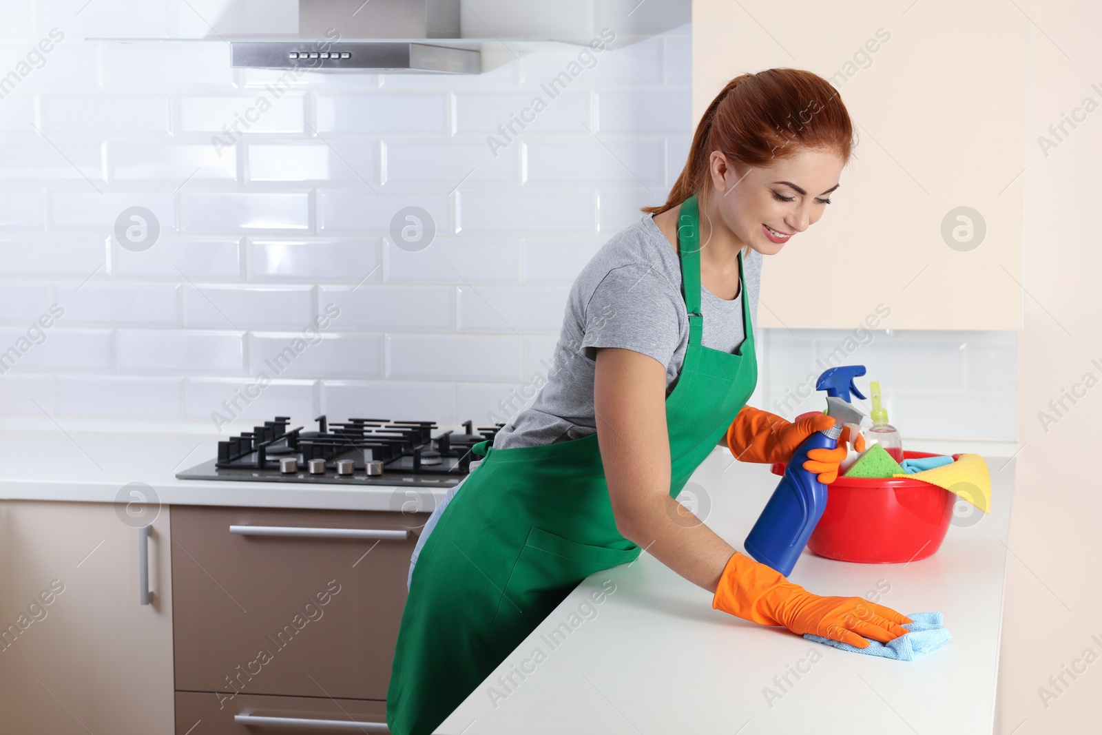 Photo of Woman in protective gloves cleaning kitchen table with rag, indoors