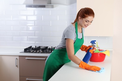 Woman in protective gloves cleaning kitchen table with rag, indoors