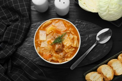 Photo of Tasty cabbage soup with meat, carrot and dill served on black wooden table, flat lay
