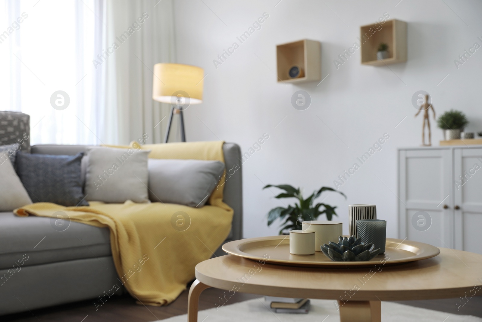 Photo of Wooden table with candles and tray near sofa in living room. Interior design