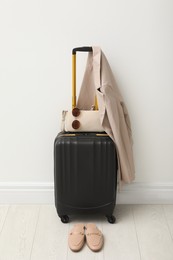 Photo of Suitcase packed for trip, shoes, jacket and accessories near white wall indoors