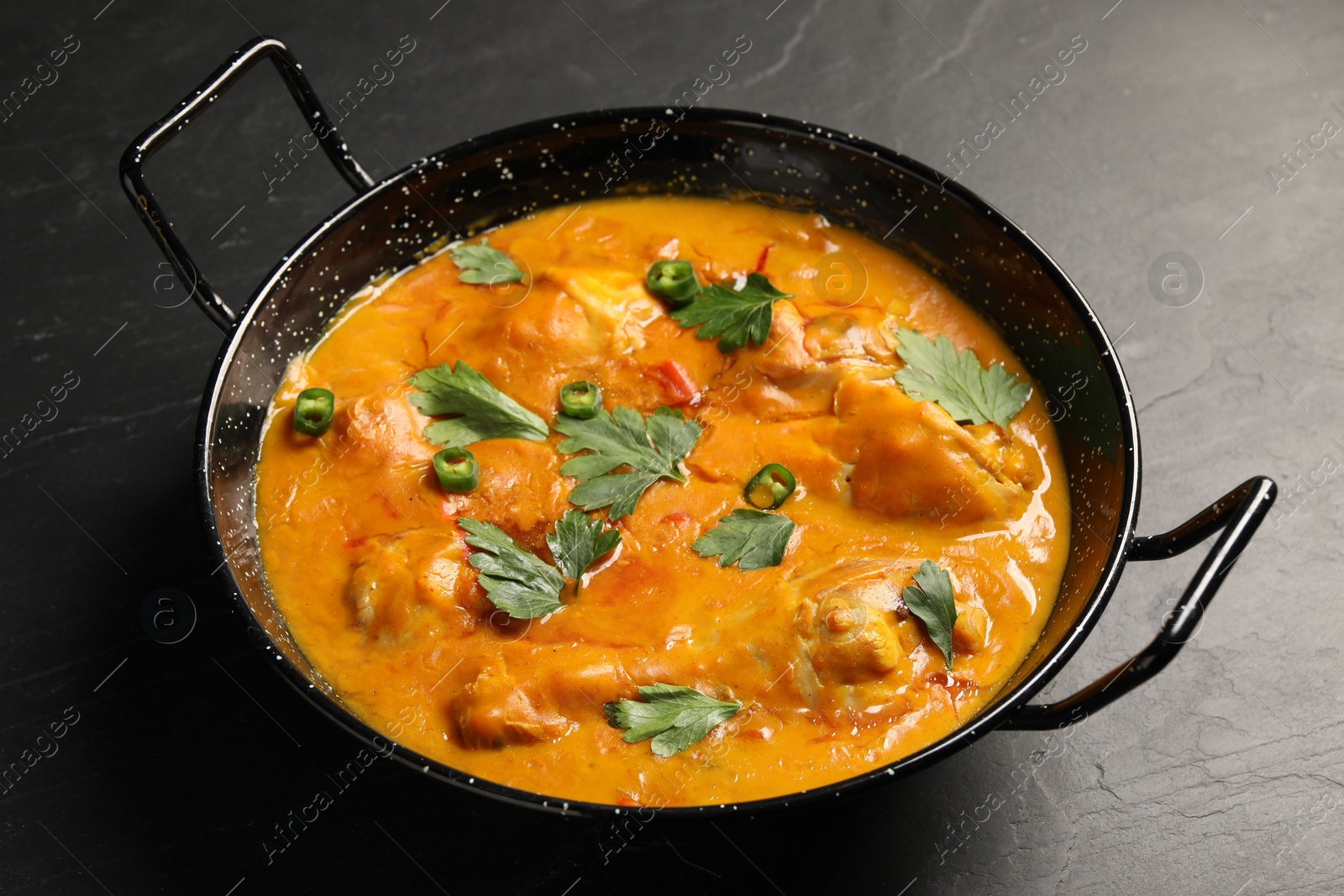 Photo of Tasty chicken curry with parsley and pepper on black textured table