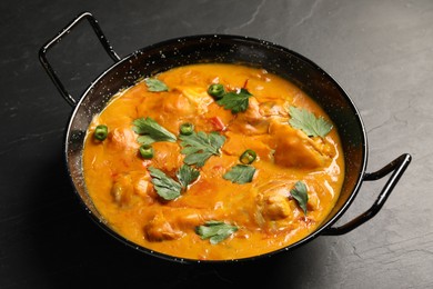 Tasty chicken curry with parsley and pepper on black textured table