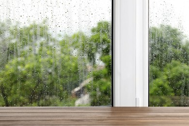 Photo of Empty wooden table near window on rainy day. Space for text