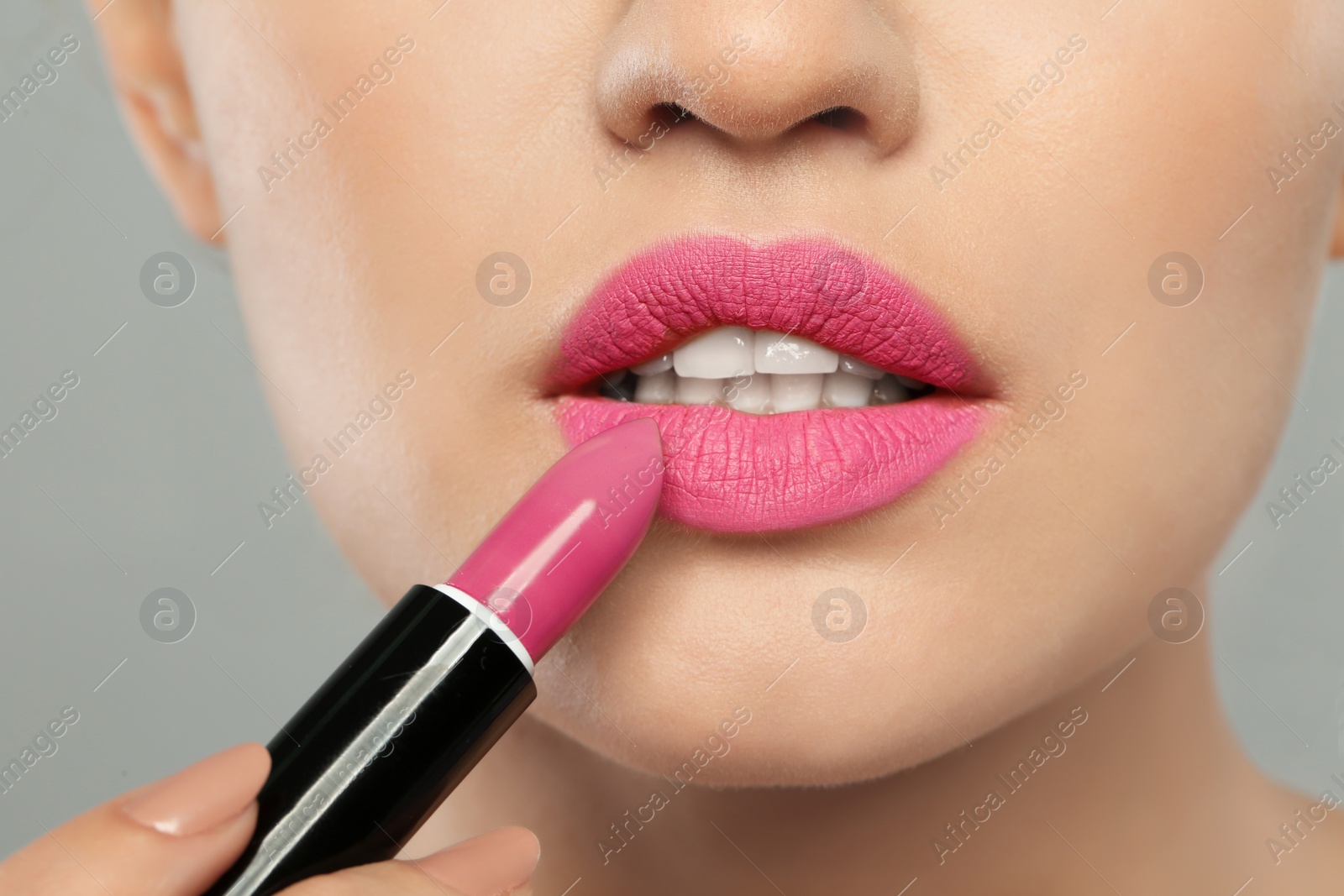 Photo of Young woman applying beautiful lipstick on gray background, closeup