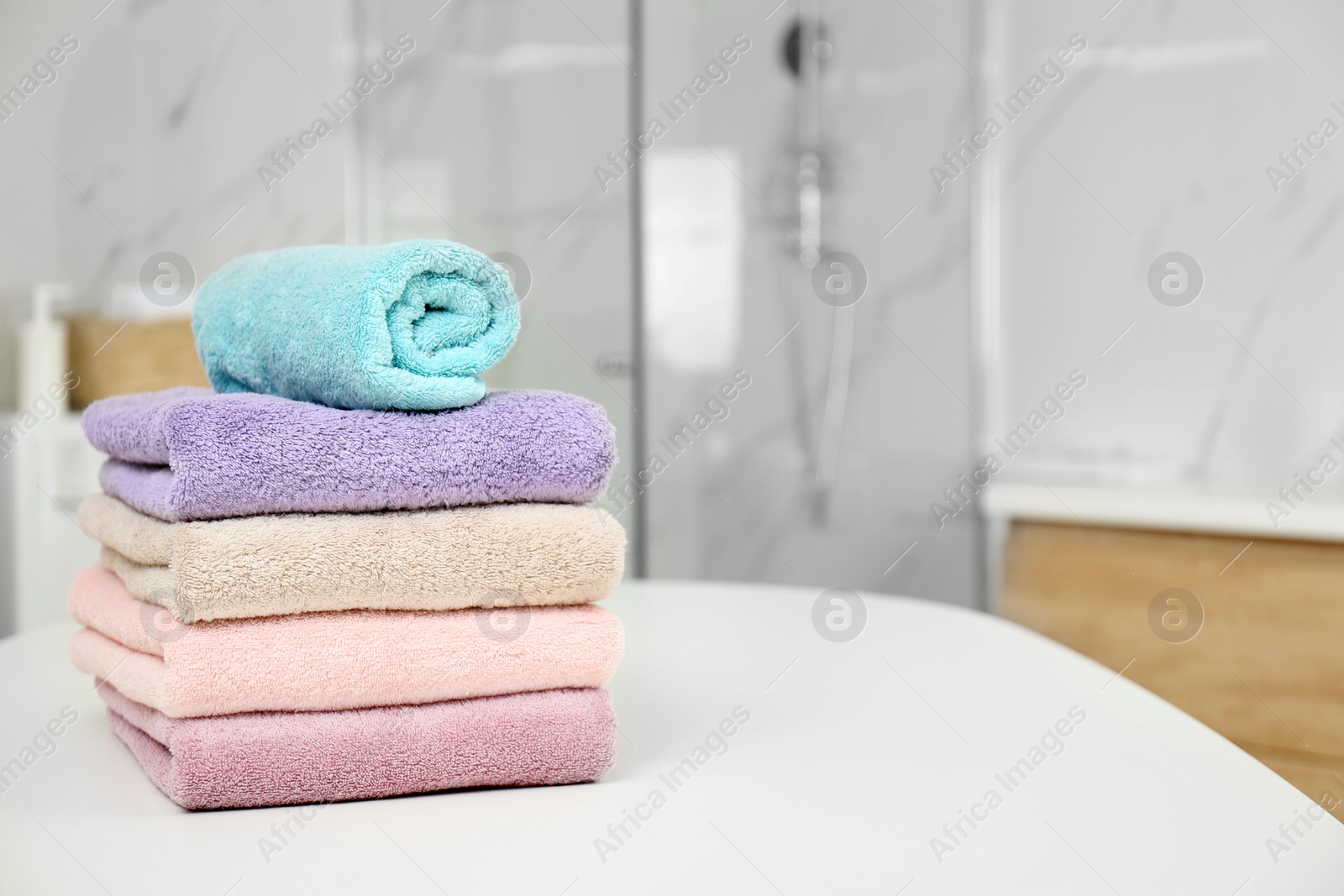 Photo of Stack of color towels on white table in bathroom. Space for text