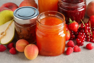 Photo of Jars with different jams and fresh fruits on grey table