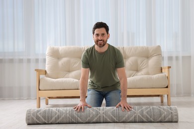 Photo of Smiling man unrolling carpet with beautiful pattern on floor in room