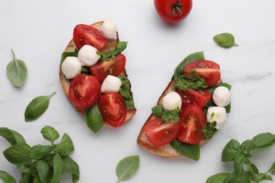 Photo of Delicious Caprese sandwiches with mozzarella, tomatoes, basil and pesto sauce on white marble table, flat lay