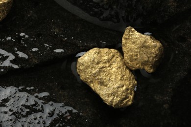 Photo of Shiny gold nuggets on wet stone, flat lay. Space for text